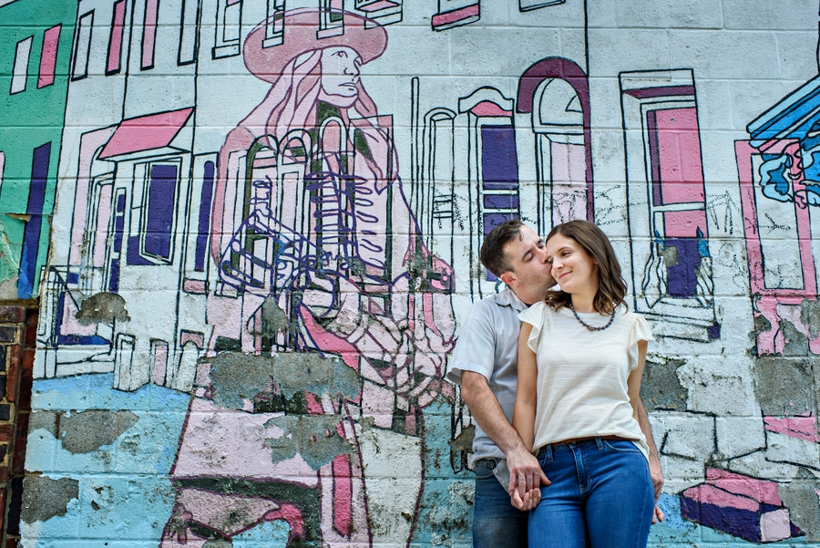 A couple kiss in front of a mural of Ben Franklin in their fishtown engagement session.